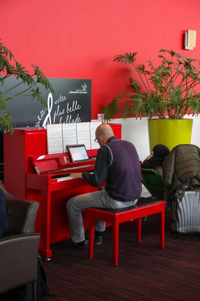 파리, 프랑스-4 월 2016: 공항에서 빨간 피아노를 연주 하는 안경에 대머리 남자 샤를 드골 공항 라운지 스톡 이미지