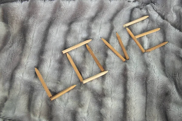 Gümüş gri tüylü faux kürk battaniye arka plan üzerinde ahşap kalemler çapraz yazılı aşk kelime yapılmış