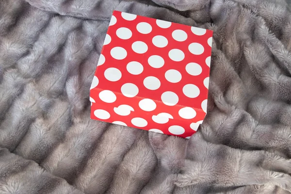 Big red gift box on the silver gray fluffy faux fur blanket background