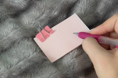 Genç kız pembe kalem tutun ve gümüş gri tüylü faux kürk battaniye arka plan üzerinde pembe metal kelepçe Kırtasiye ile hafif pembe etiket üzerine yazmak