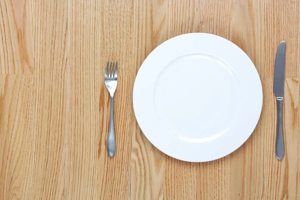 Tenedor de comedor y cuchillo al lado de un plato en una mesa de madera con copia s — Foto de Stock