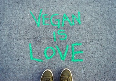 Pov yeşil casual ayakkabı ile çimento kaldırımda metin kelime Vegan Is Love yeşil tebeşir yazı.