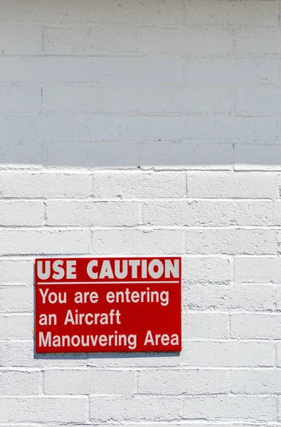 Aircraft manouvering red and white warning sign hung on painted brick wall.