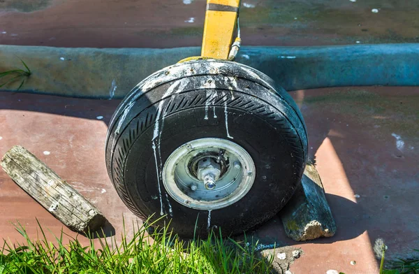 Old small single engine airplane wheel and wooden chocks on parking pad.