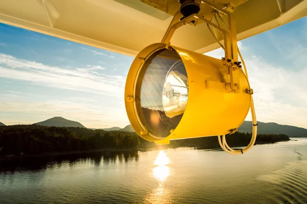 Large yellow marine search light hanging from exterior of cruise ship, backlit by warm afternoon sun. — Stock Photo, Image