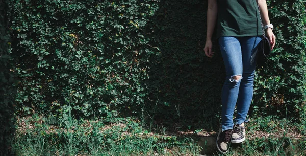 Vrouwelijke Wachten Benen Jeans Leunend Tegen Een Muur Van Gras — Stockfoto