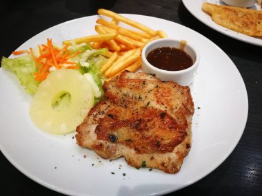 Siyah bir tablo üzerinde beyaz bir tabak içinde tavuk biftek