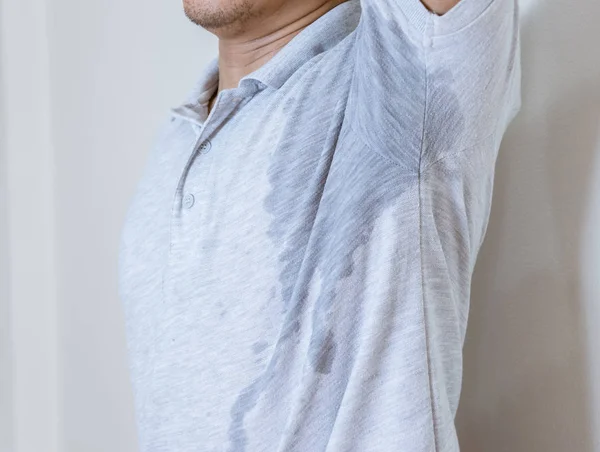 Man with sweat stain on clothes against, using deodorant