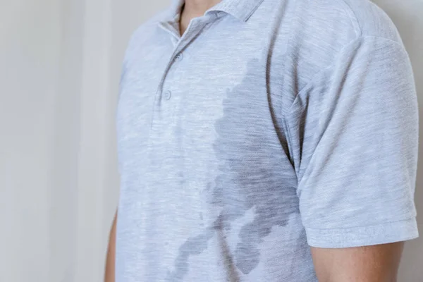 Man with sweat stain on clothes against, using deodorant