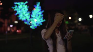 güzel kız haberleri smartphone içinde akşam park, parlak yangınları izliyor