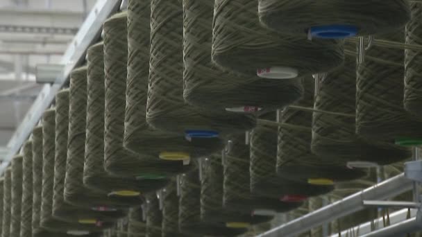 Factory for the production of clothing fabrics. Large spools of thread feed the carpet. — Stock Video