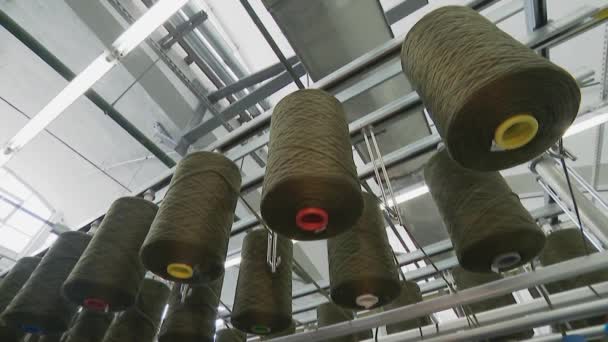 Factory for the production of clothing fabrics. Large spools of thread feed the carpet. — Stock Video