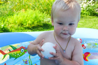 Çocuk doğada bir şişme havuzunda yüzüyor.