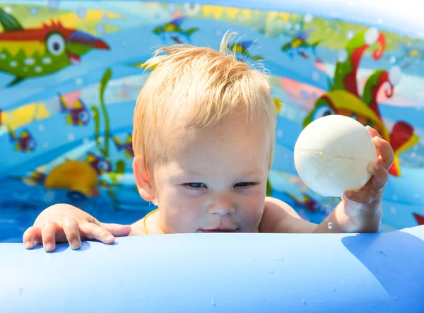 Çocuk doğada bir şişme havuzunda yüzüyor.