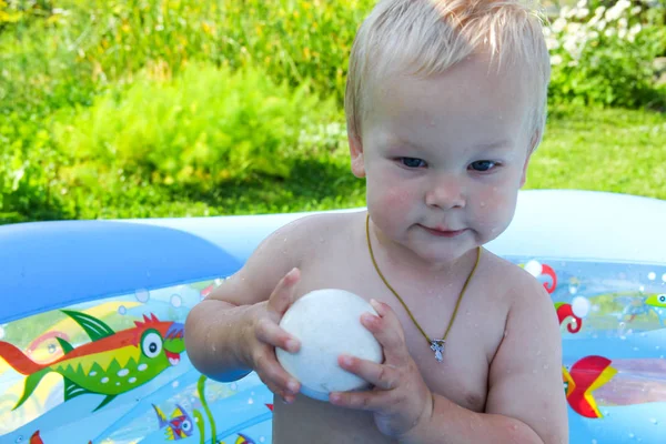 Çocuk doğada bir şişme havuzunda yüzüyor.