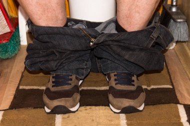 Adam tuvalette pantolon aşağı spor ayakkabıları ile oturan.