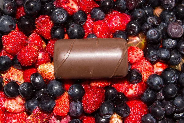 Wild berries with chocolates.Background of blueberries,strawberries and candy.
