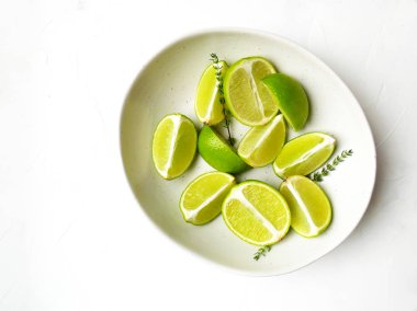 Beyaz doku arka planda taze kireç ve kekik. Tabakta minimalist otlar ve meyveler