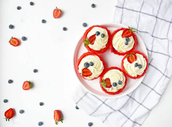 Beyaz doku ve trendy mutfak havlusu üzerinde krem peynir, çilek ve yaban mersini ile Cupcakes.