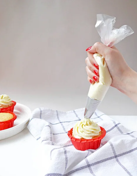 Krem peynir şekerleme çantası ile şefin ellerini kapatın. Beyaz arka planda cupcakes. Pişirme süreci