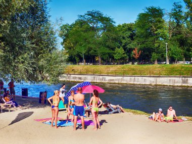Kaloşvar, Romanya-11 Ağustos 2018: On çocuklu aileler sıcak kum plaj nehrin yanında onların deri güneşlenme