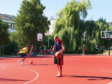 Kaloşvar, Romanya-11 Ağustos 2018: Mutlu gençler ve güneşli yaz günü sahada basketbol oynarken bir yetişkin