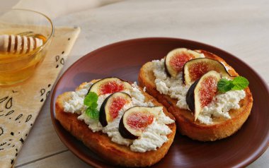 Ahşap masa üzerinde keçi peyniri, incir dilimleri, bal ve otlar ile tepesinde Crostini tost