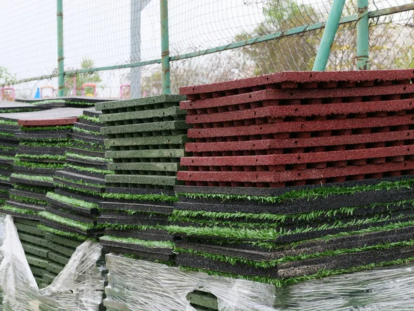 Stack of rubber floor tile mats and artificial turf grass rug tiles for elastic safety flooring. Eco safety surfacing mats are a low cost solution and reduce the risk of injury caused by falls on playgrounds, sport fields and recreational facilities.