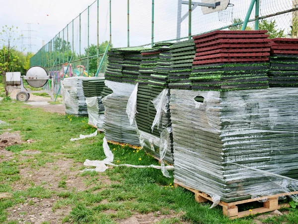 Stack of rubber floor tile mats and artificial turf grass rug tiles for elastic safety flooring. Eco safety surfacing mats are a low cost solution and reduce the risk of injury caused by falls on playgrounds, sport fields and recreational facilities.