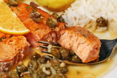 Tasty bite of salmon piccata with creamy lemon caper butter sauce on fork with rice, closeup. clipart