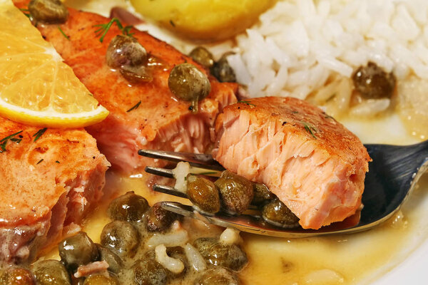 Tasty bite of salmon piccata with creamy lemon caper butter sauce on fork with rice, closeup.