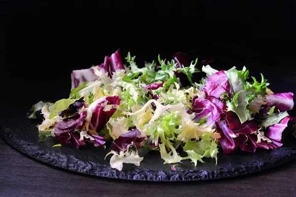 Mix of bitter-leafed vegetables, endive, radicchio, frisee and escarole leaf chicory salad over black slate platter (Cichorium endivia)
