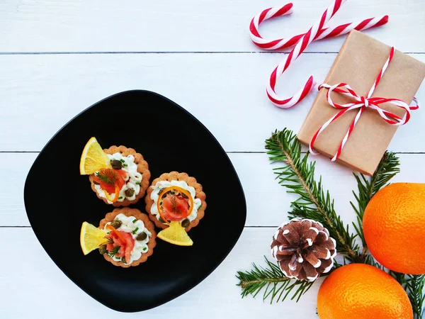 圣诞节背景与熏制的三文鱼罐头在黑色盘子 糖果棒 橘子和冷杉树枝上的饼干上 — 图库照片