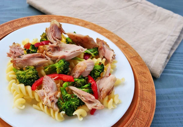 Макароны с куриным мясом, брокколи и овощами на белой тарелке — стоковое фото