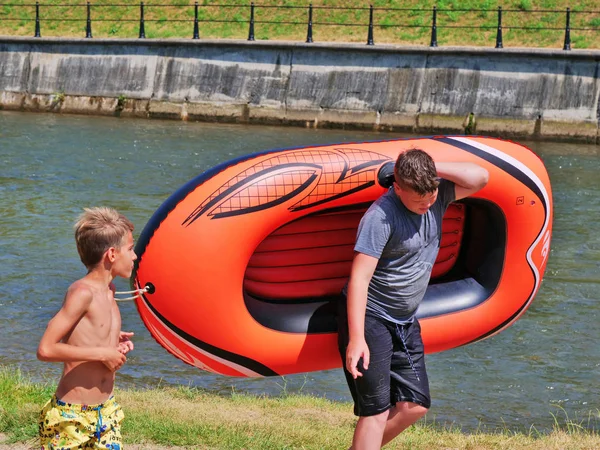 Dos jóvenes llevan una balsa inflable a lo largo del río —  Fotos de Stock
