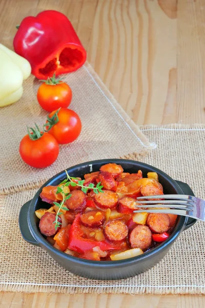 Gemüseeintopf mit Wurstscheiben in schwarzer Schüssel über Holztisch — Stockfoto