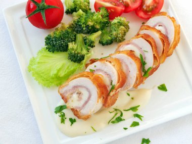 Kremalı beyaz sos ve sebzelerle dilimlenmiş tavuk cordon bleu, üst manzara, düz yatış.