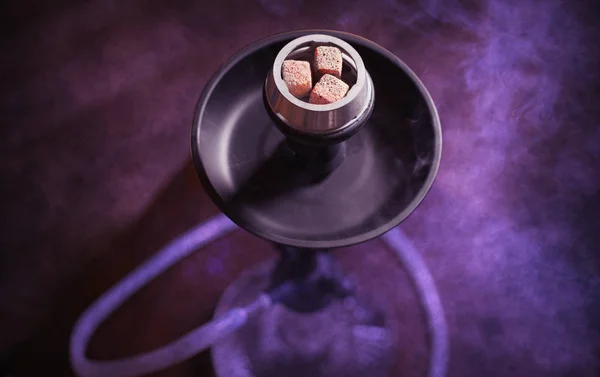 Photo of burning coals in a hookah on a background of smoke and purple light