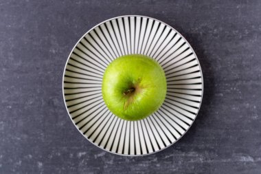 Yukarıdan mermer arka plan üzerinde bir tabak üzerinde bir Taze yeşil granny Smith Apple
