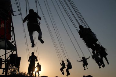 Gençler dönme dolap ve gün batımı arka plan üzerinde durmak devinim içinde sallanan atlıkarınca silüeti