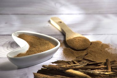 Beyaz ahşap arka plan-Cinnamomum verum izole toz bir tahta kaşık ve tarçın, tarçın