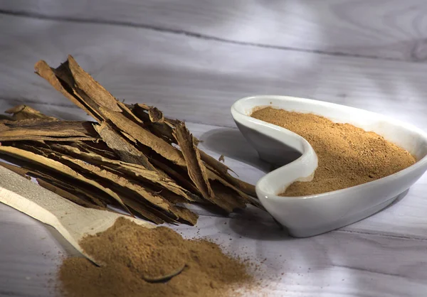 Beyaz ahşap arka plan-Cinnamomum verum izole toz bir tahta kaşık ve tarçın, tarçın