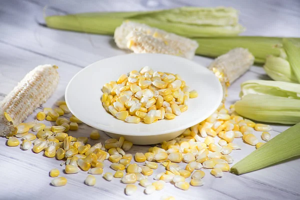 maize-cob and yellow corn kernels in white glass vase on white wooden background- zea mays