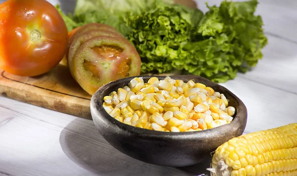 maize-cob and yellow corn grains in clay pot on white wooden background- zea mays