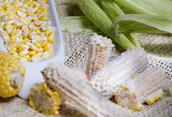 maize-cob and yellow corn kernels in white glass vase on white wooden background - zea mays