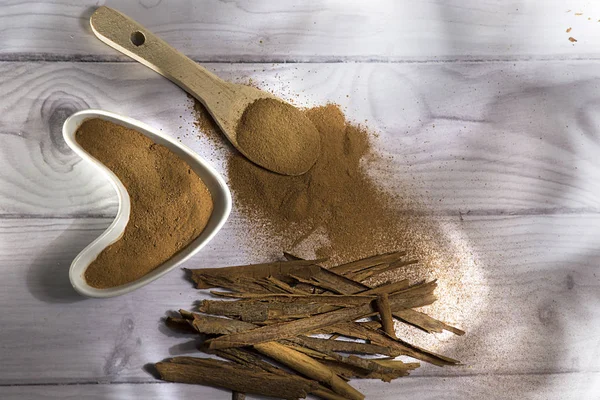 Beyaz ahşap arka plan-Cinnamomum verum izole toz bir tahta kaşık ve tarçın, tarçın