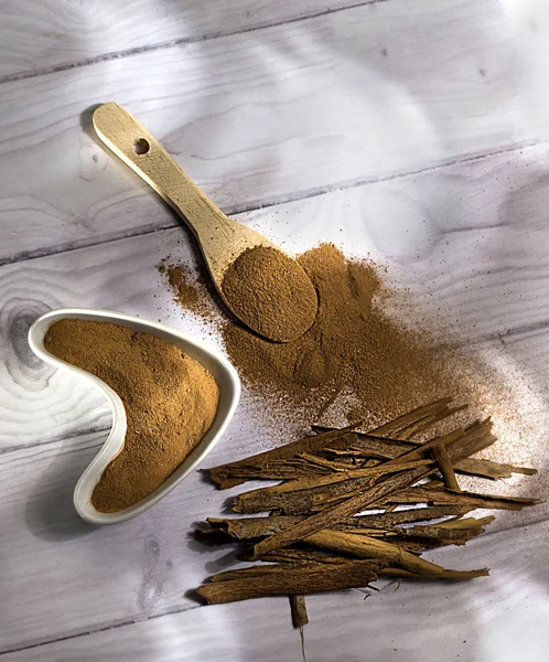 Beyaz ahşap arka plan-Cinnamomum verum izole toz bir tahta kaşık ve tarçın, tarçın