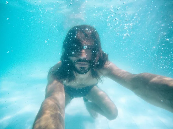 Çekici bir genç adam kameraya bakarak havuzda sular altında