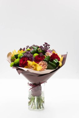 Gül, karanfil ve orkide paket parlak bir buket. Bir cam vazo içinde hafif bir arka plan üzerinde