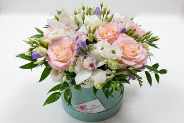 Beyaz ve pembe güller ve orkide yeşil ile narin buket gök mavisi renkli bir şapka kutusunda hafif bir arka plan üzerinde bırakır.